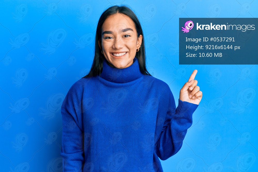 Young asian woman wearing casual winter sweater with a big smile on face, pointing with hand finger to the side looking at the camera. 