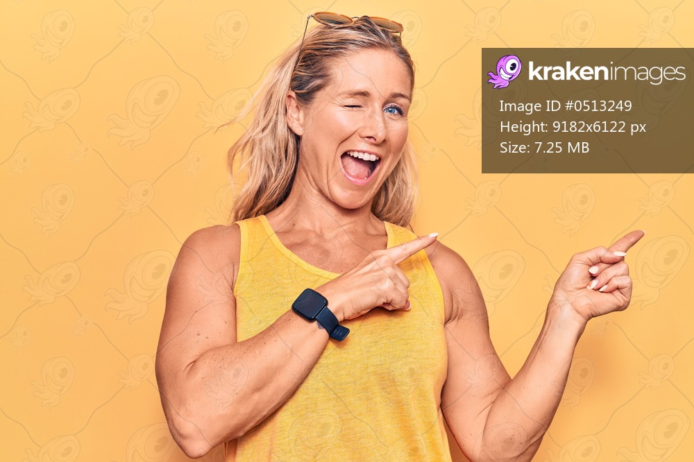 Middle age caucasian blonde woman wearing casual summer clothes and sunglasses smiling and looking at the camera pointing with two hands and fingers to the side. 