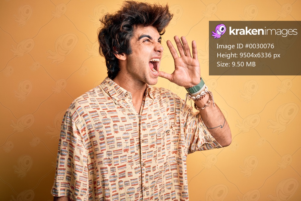 Young handsome man on vacation wearing summer shirt over isolated yellow background shouting and screaming loud to side with hand on mouth. Communication concept.