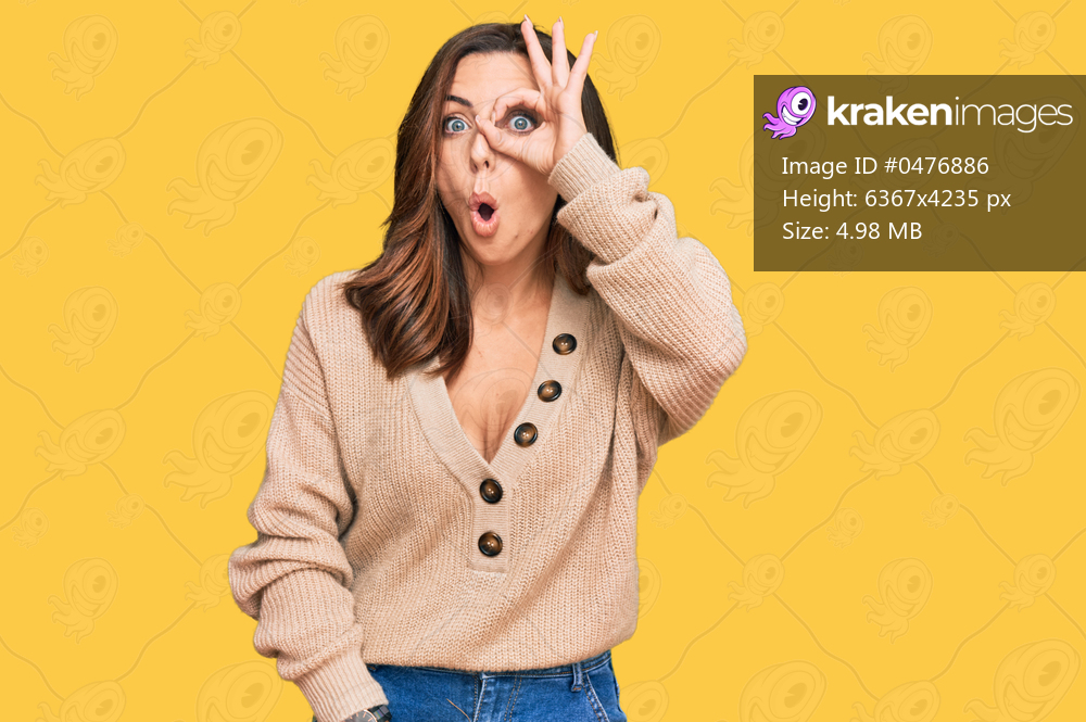 Young brunette woman wearing casual winter sweater doing ok gesture shocked with surprised face, eye looking through fingers. unbelieving expression. 