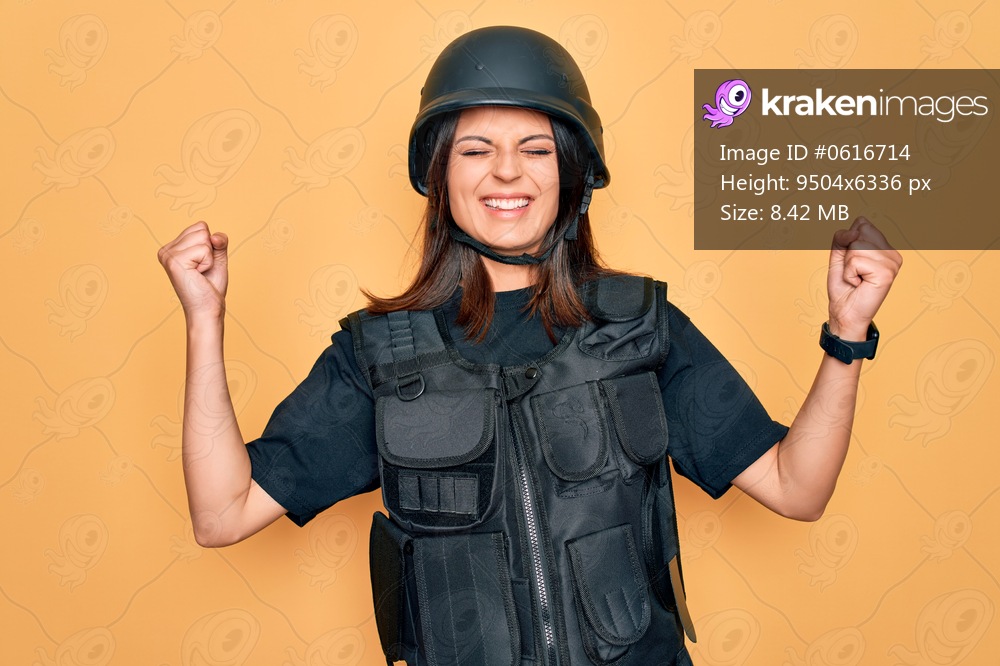 Young beautiful brunette soldier woman wearing bulletproof and security helmet very happy and excited doing winner gesture with arms raised, smiling and screaming for success. Celebration concept.