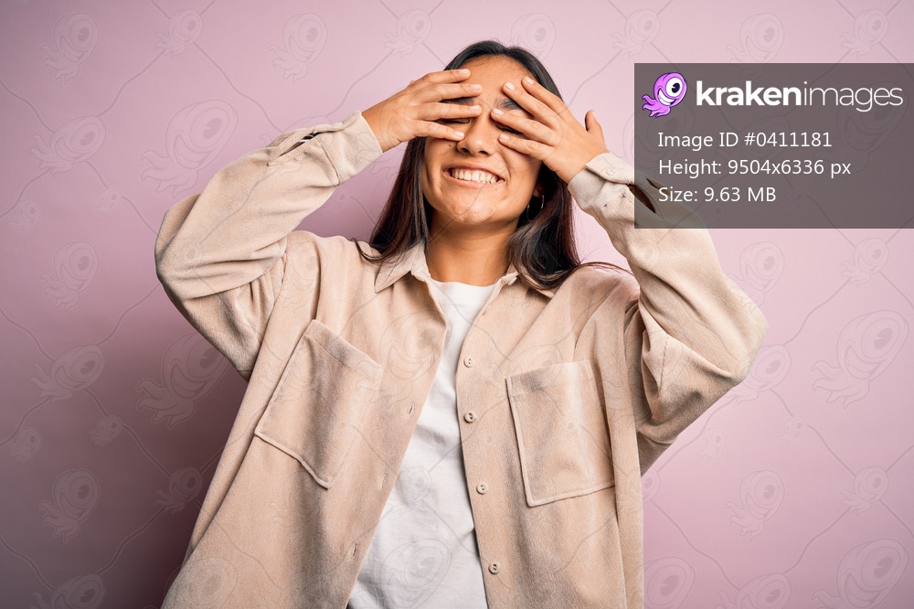 Young beautiful asian woman wearing casual shirt standing over pink background covering eyes with hands smiling cheerful and funny. Blind concept.