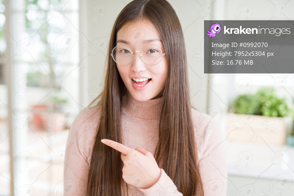 Beautiful Asian woman wearing glasses cheerful with a smile of face pointing with hand and finger up to the side with happy and natural expression on face