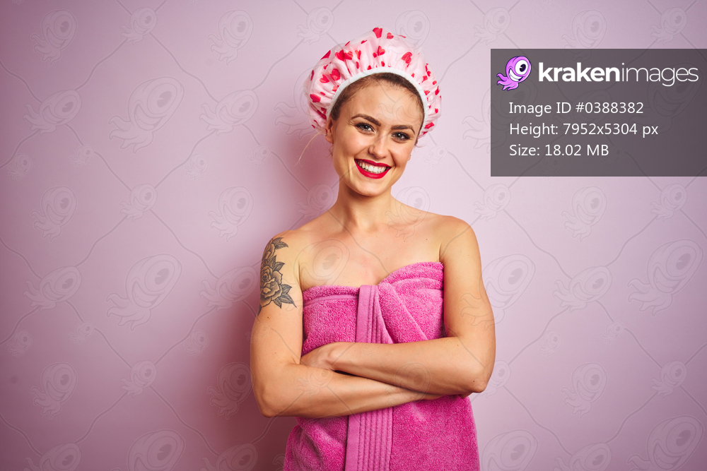 Young beautiful woman wearing towel and bath hat after shower over pink isolated background happy face smiling with crossed arms looking at the camera. Positive person.