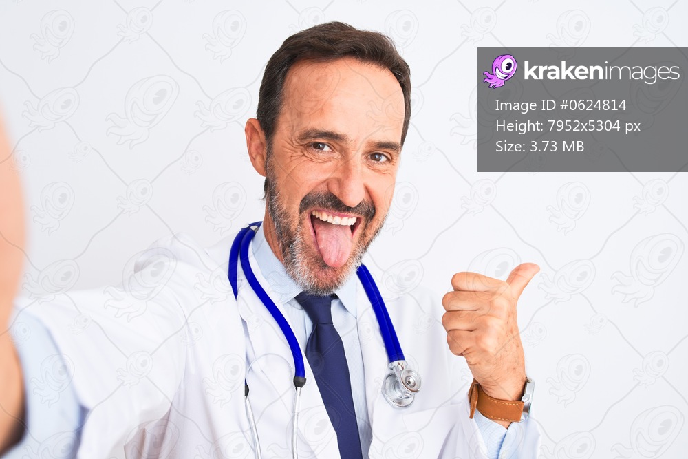 Middle age doctor man wearing stethoscope make selfie over isolated white background pointing and showing with thumb up to the side with happy face smiling