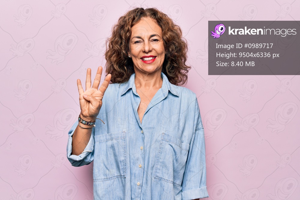 Middle age beautiful woman wearing casual denim shirt standing over pink background showing and pointing up with fingers number four while smiling confident and happy.