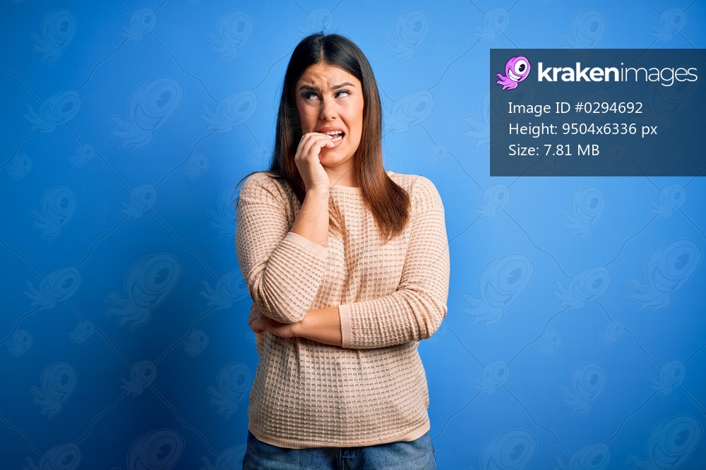 Young beautiful woman wearing casual sweater over blue background looking stressed and nervous with hands on mouth biting nails. Anxiety problem.