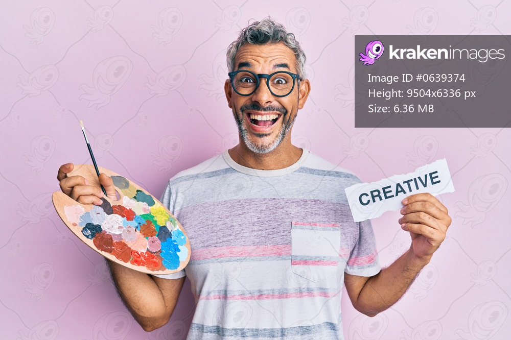 Middle age grey-haired man holding palette and creative message paper celebrating crazy and amazed for success with open eyes screaming excited. 