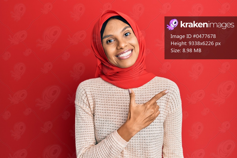 Young african american woman wearing traditional islamic hijab scarf smiling cheerful pointing with hand and finger up to the side 