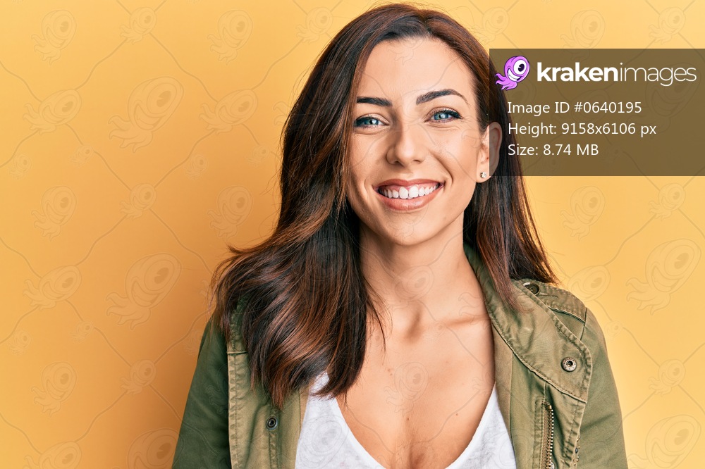 Young brunette woman wearing casual clothes over yellow background smiling with a happy and cool smile on face. showing teeth. 