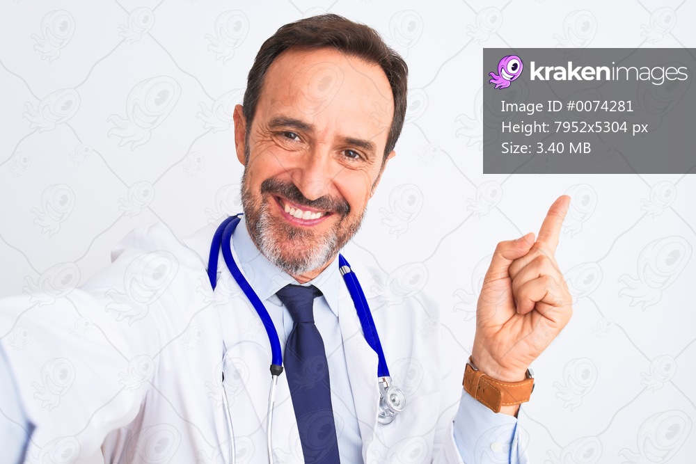 Middle age doctor man wearing stethoscope make selfie over isolated white background very happy pointing with hand and finger to the side