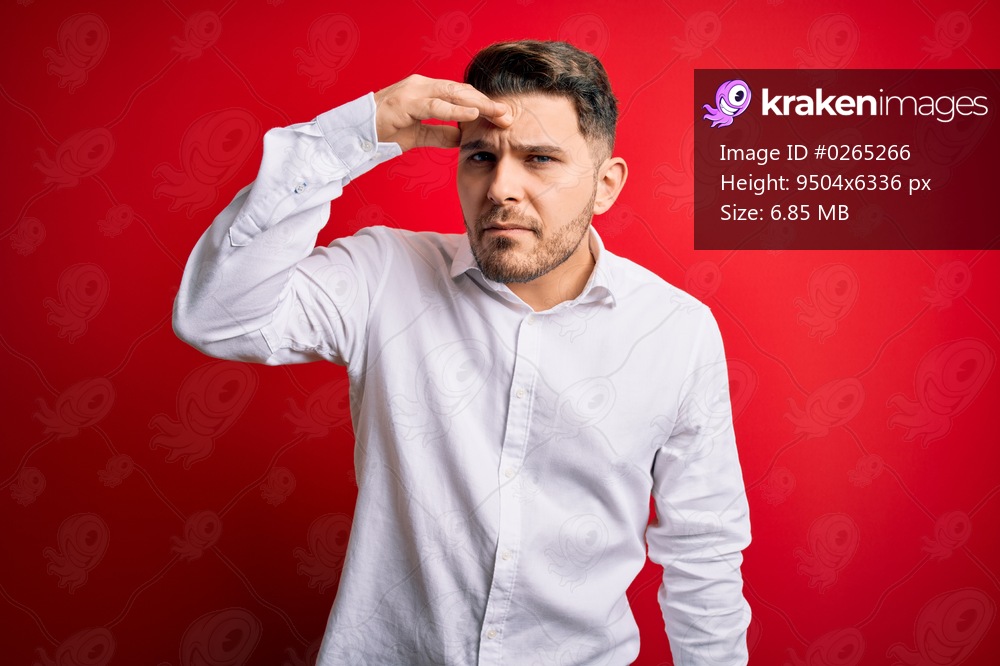 Young business man with blue eyes wearing elegant shirt standing over red isolated background pointing unhappy to pimple on forehead, ugly infection of blackhead. Acne and skin problem