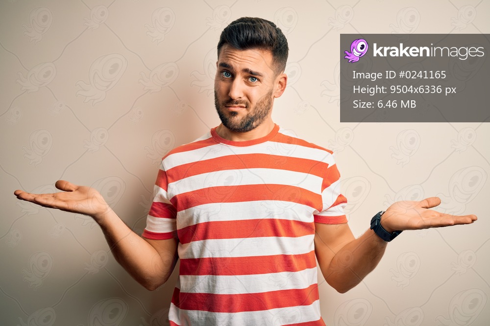 Young handsome man wearing casual striped t-shirt standing over isolated white background clueless and confused with open arms, no idea concept.