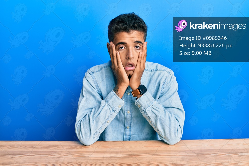 Young handsome african american man wearing casual clothes sitting on the table tired hands covering face, depression and sadness, upset and irritated for problem 