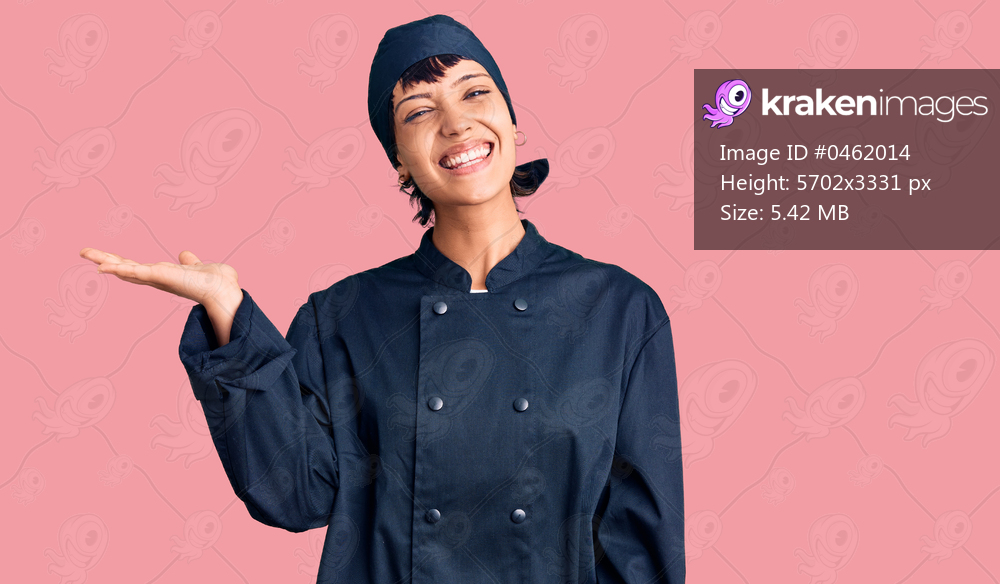 Young brunette woman with short hair wearing professional cook uniform smiling cheerful presenting and pointing with palm of hand looking at the camera. 