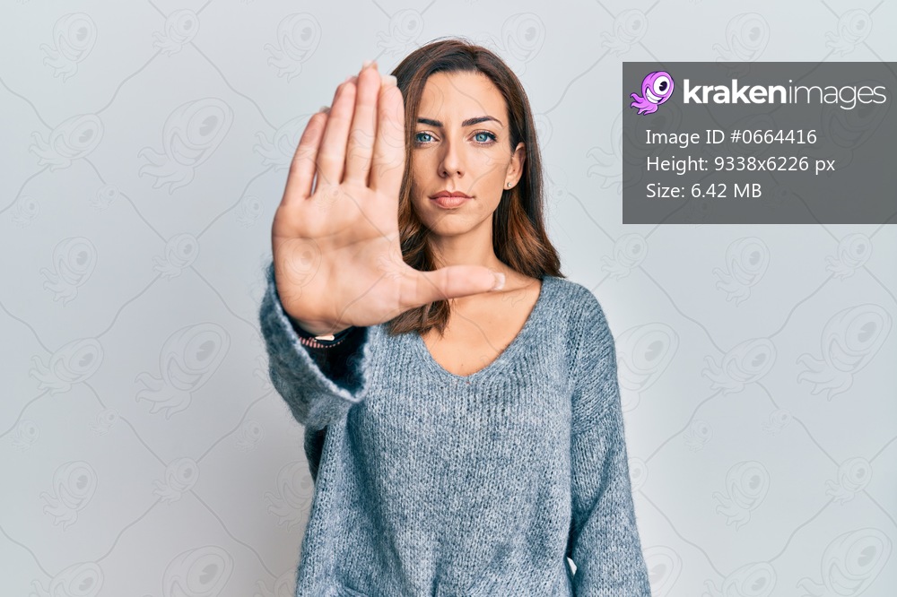 Young brunette woman wearing casual winter sweater doing stop sing with palm of the hand. warning expression with negative and serious gesture on the face. 