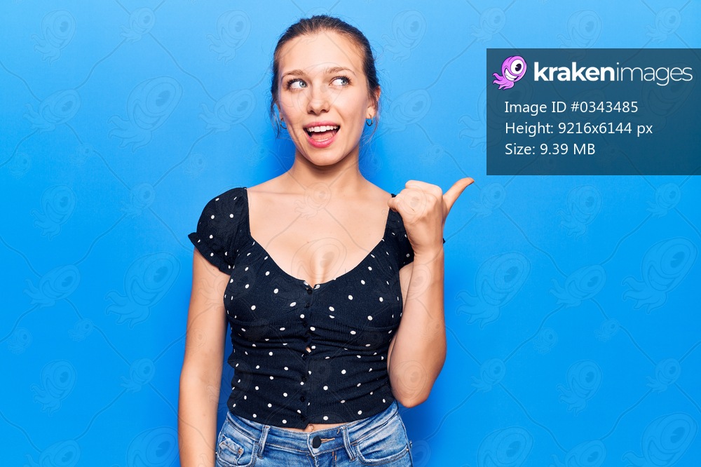 Young blonde woman wearing casual clothes pointing thumb up to the side smiling happy with open mouth 
