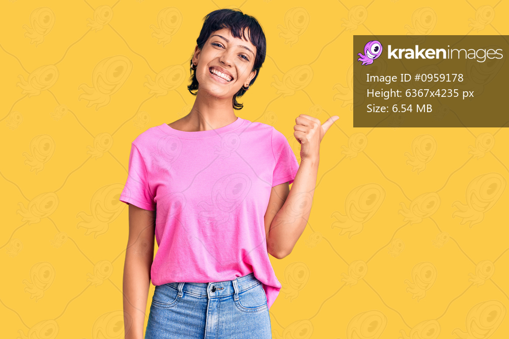 Young brunette woman with short hair wearing casual clothes smiling with happy face looking and pointing to the side with thumb up. 