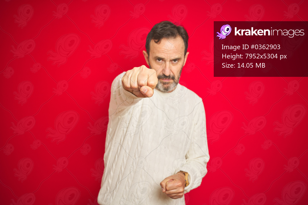 Handsome middle age senior man with grey hair over isolated red background Punching fist to fight, aggressive and angry attack, threat and violence