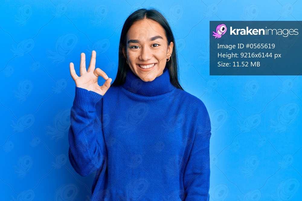 Young asian woman wearing casual winter sweater smiling positive doing ok sign with hand and fingers. successful expression. 