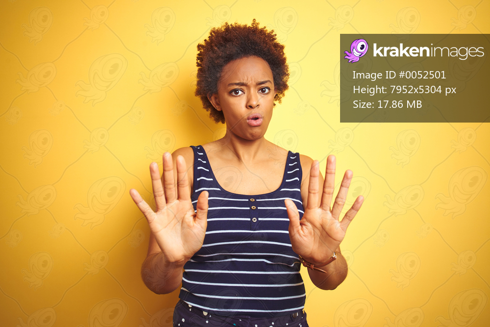 Beauitul african american woman wearing summer t-shirt over isolated yellow background Moving away hands palms showing refusal and denial with afraid and disgusting expression. Stop and forbidden.
