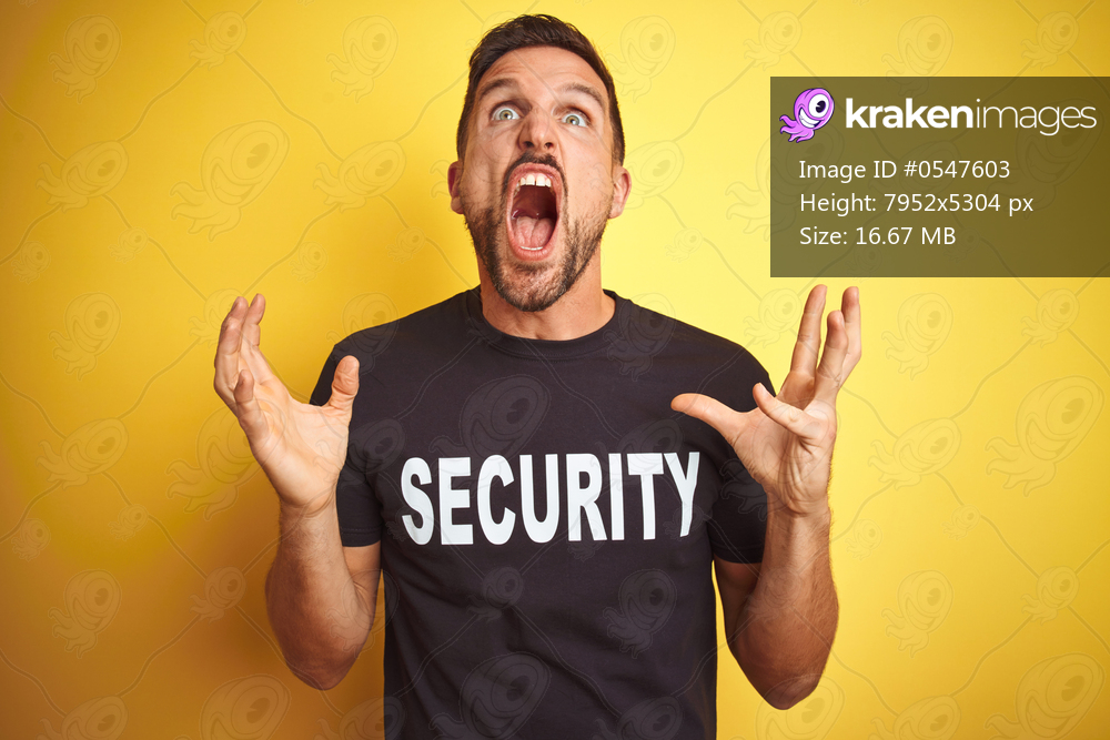 Young safeguard man wearing security uniform over yellow isolated background crazy and mad shouting and yelling with aggressive expression and arms raised. Frustration concept.
