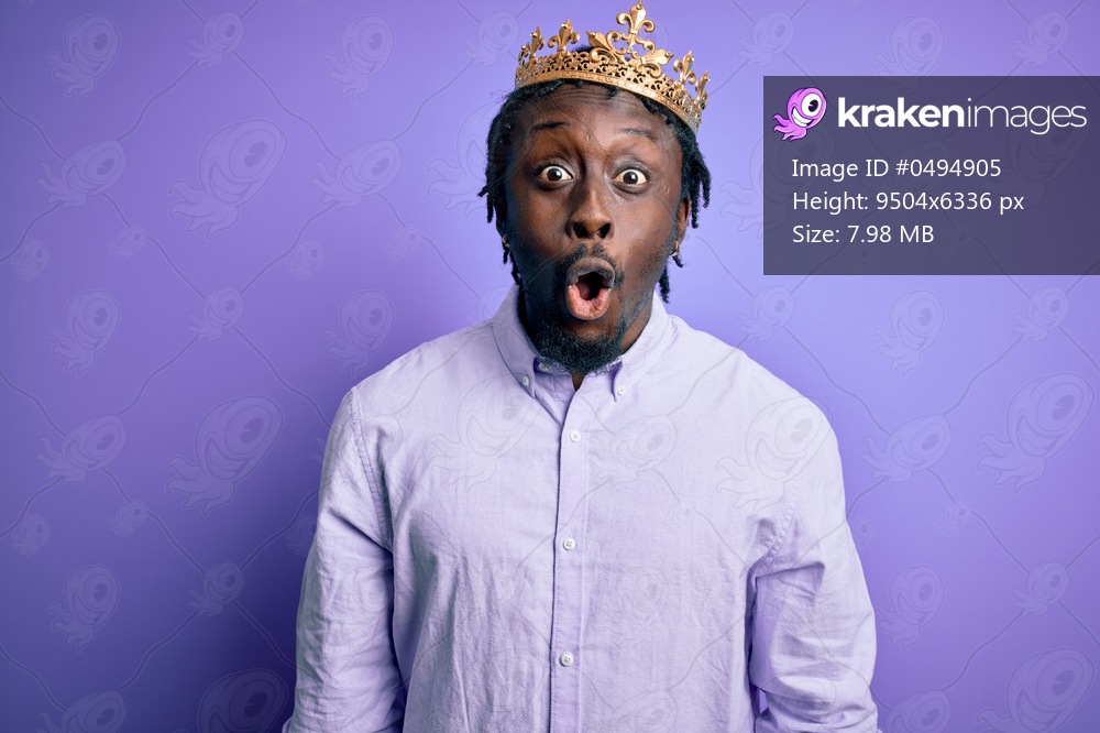 Young african american man wearing golden crown of king over isolated purple background afraid and shocked with surprise expression, fear and excited face.