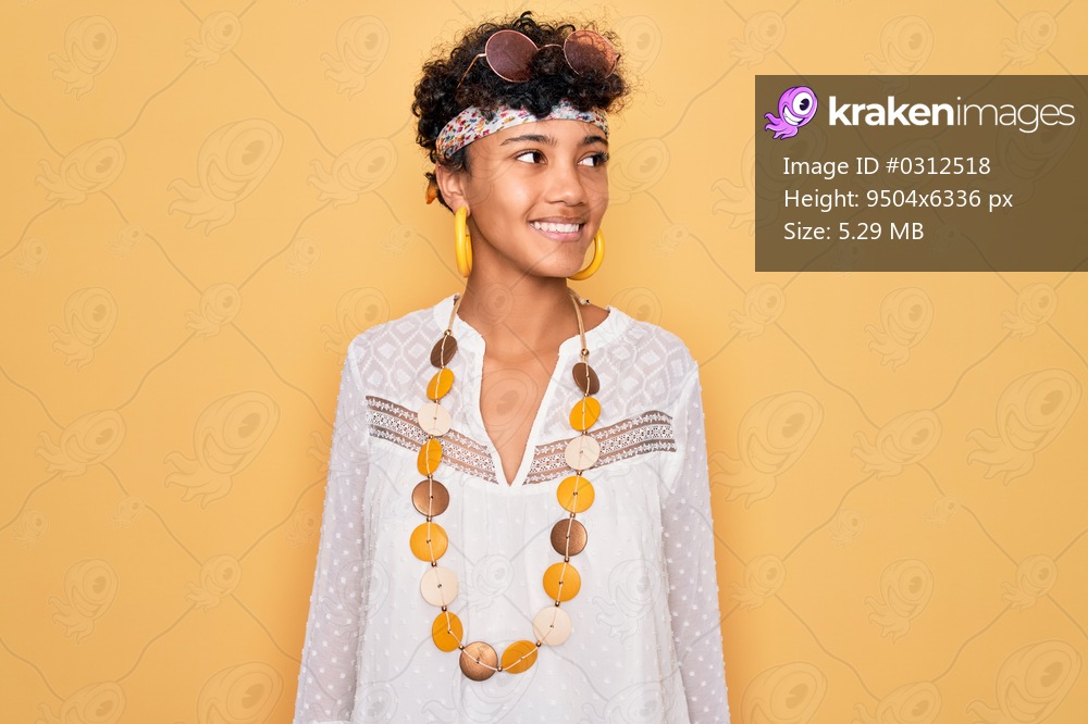 Young beautiful african american afro hippie woman wearing sunglasses and accessories looking away to side with smile on face, natural expression. Laughing confident.