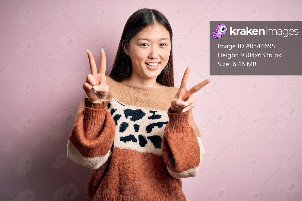 Young beautiful asian woman wearing animal print fashion sweater over pink isolated background smiling looking to the camera showing fingers doing victory sign. Number two.