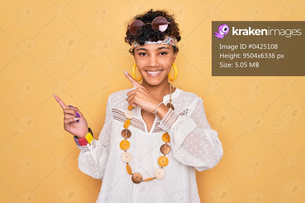 Young beautiful african american afro hippie woman wearing sunglasses and accessories smiling and looking at the camera pointing with two hands and fingers to the side.