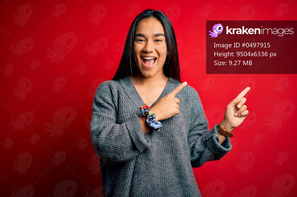 Young beautiful asian woman wearing casual sweater standing over isolated red background smiling and looking at the camera pointing with two hands and fingers to the side.