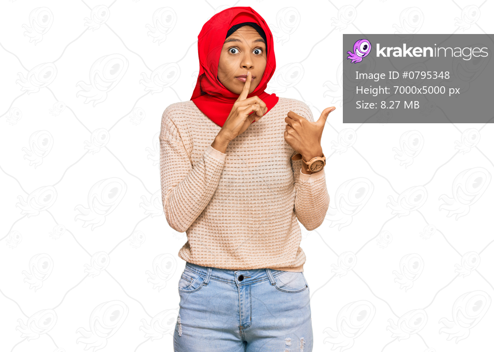 Young african american woman wearing traditional islamic hijab scarf asking to be quiet with finger on lips pointing with hand to the side. silence and secret concept. 