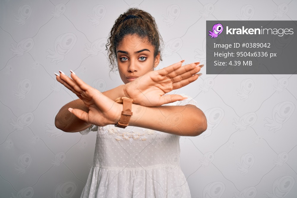 Young beautiful african american girl wearing casual t-shirt standing over white background Rejection expression crossing arms and palms doing negative sign, angry face