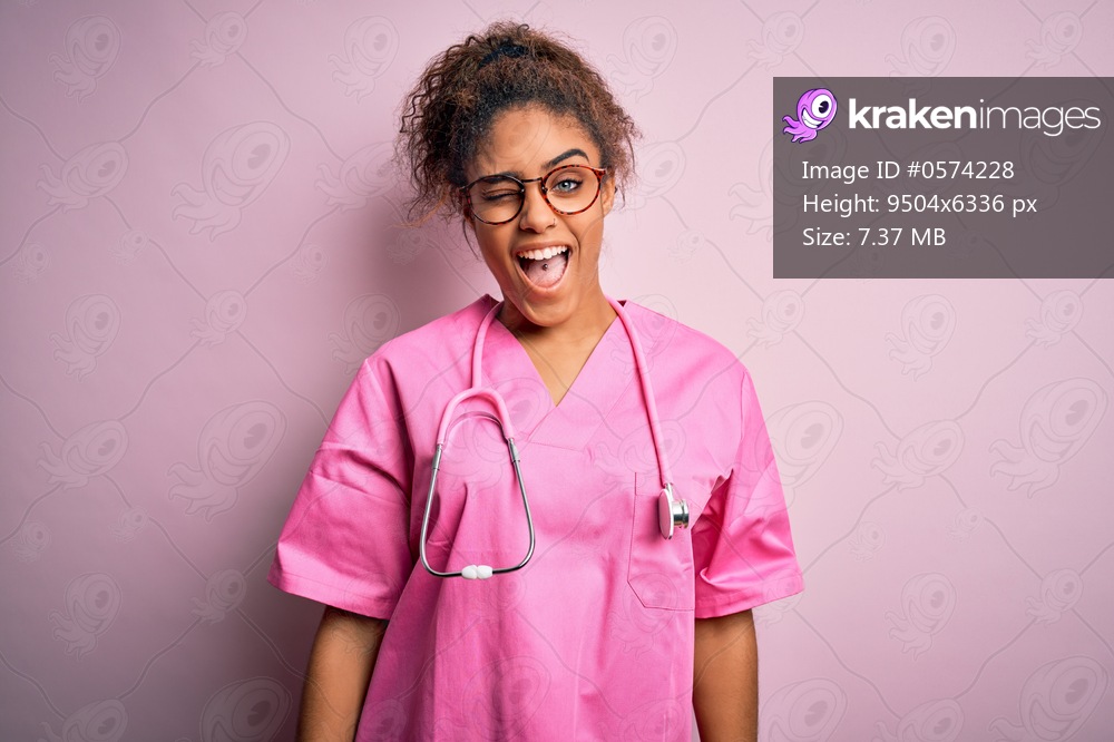 African american nurse girl wearing medical uniform and stethoscope over pink background winking looking at the camera with sexy expression, cheerful and happy face.