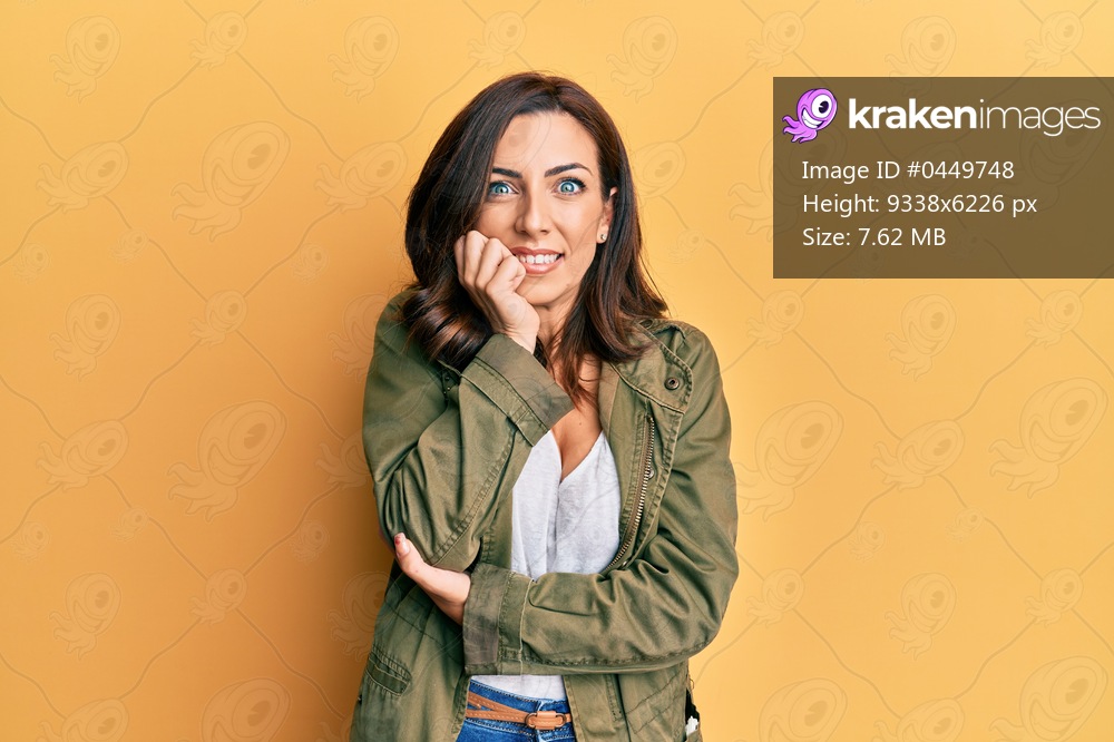 Young brunette woman wearing casual clothes over yellow background looking stressed and nervous with hands on mouth biting nails. anxiety problem. 