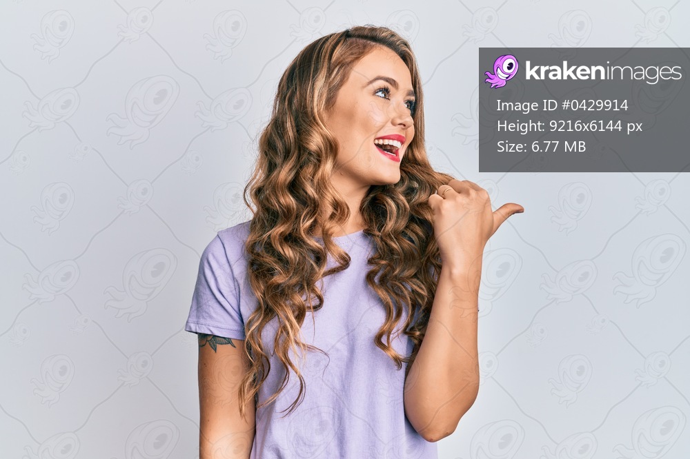 Young blonde girl wearing casual clothes pointing thumb up to the side smiling happy with open mouth 