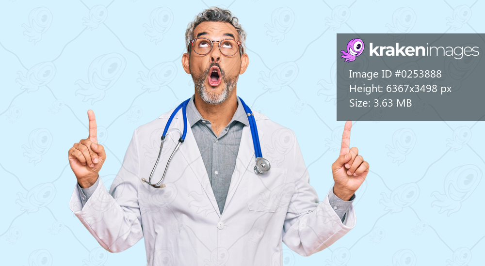Middle age grey-haired man wearing doctor uniform and stethoscope amazed and surprised looking up and pointing with fingers and raised arms. 