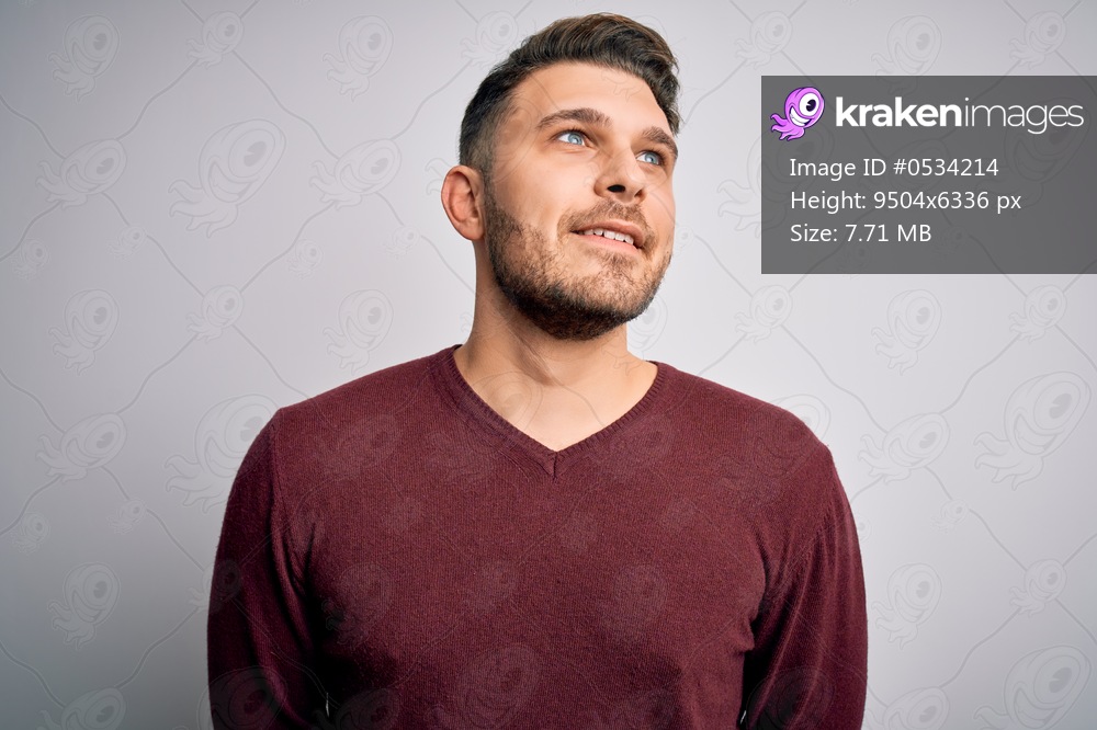 Young man with blue eyes wearing casual sweater standing over isolated background looking away to side with smile on face, natural expression. Laughing confident.