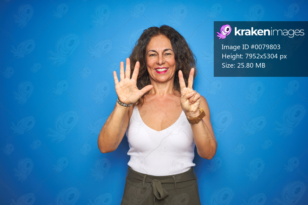 Middle age senior woman with curly hair standing over blue isolated background showing and pointing up with fingers number seven while smiling confident and happy.