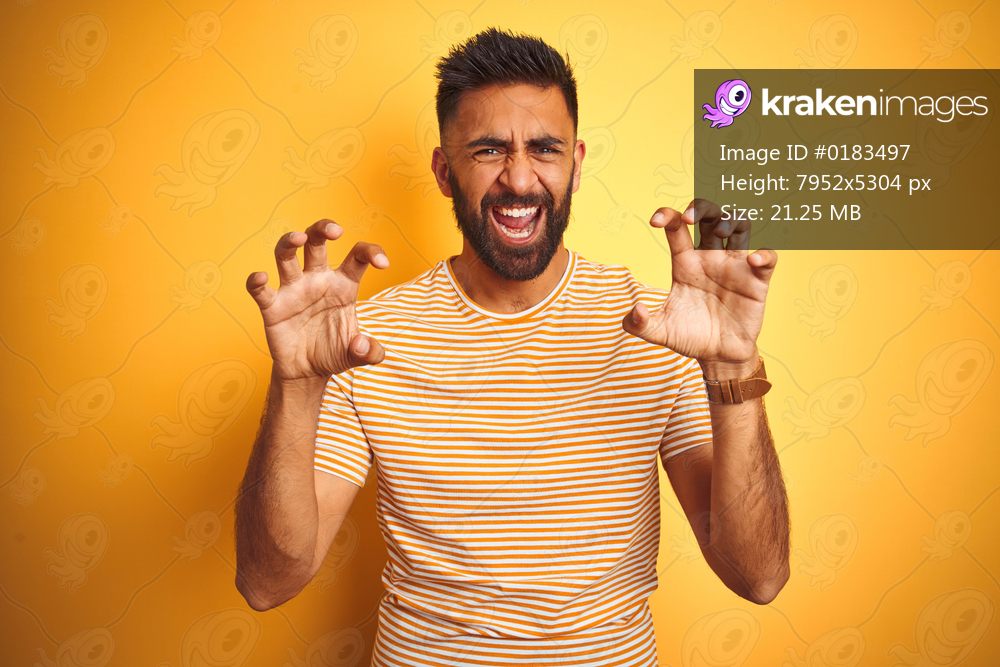 Young indian man wearing t-shirt standing over isolated yellow background smiling funny doing claw gesture as cat, aggressive and sexy expression
