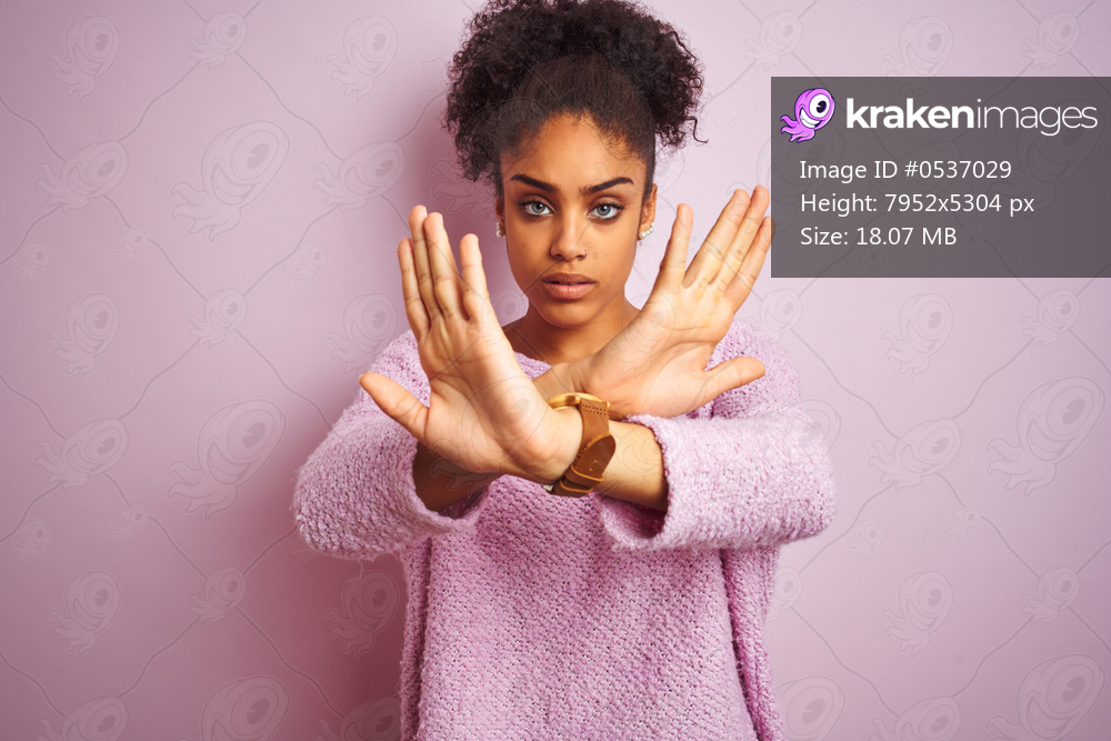 Young african american woman wearing winter sweater standing over isolated pink background Rejection expression crossing arms and palms doing negative sign, angry face