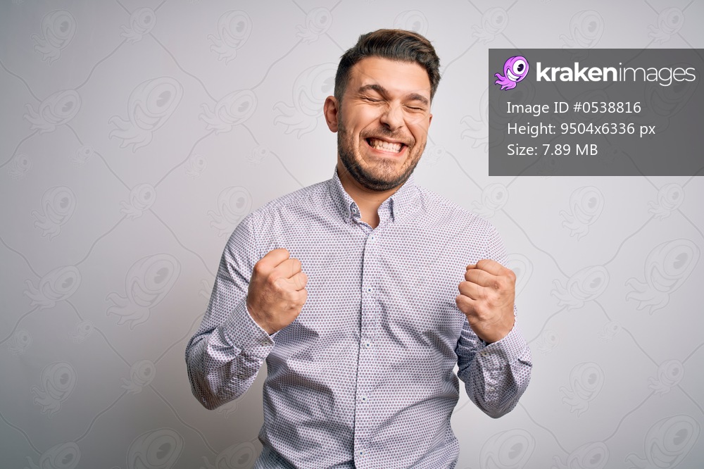 Young business man with blue eyes standing over isolated background excited for success with arms raised and eyes closed celebrating victory smiling. Winner concept.