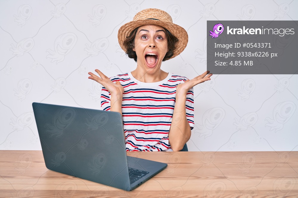 Young hispanic woman working with laptop sitting on the table celebrating mad and crazy for success with arms raised and closed eyes screaming excited. winner concept 