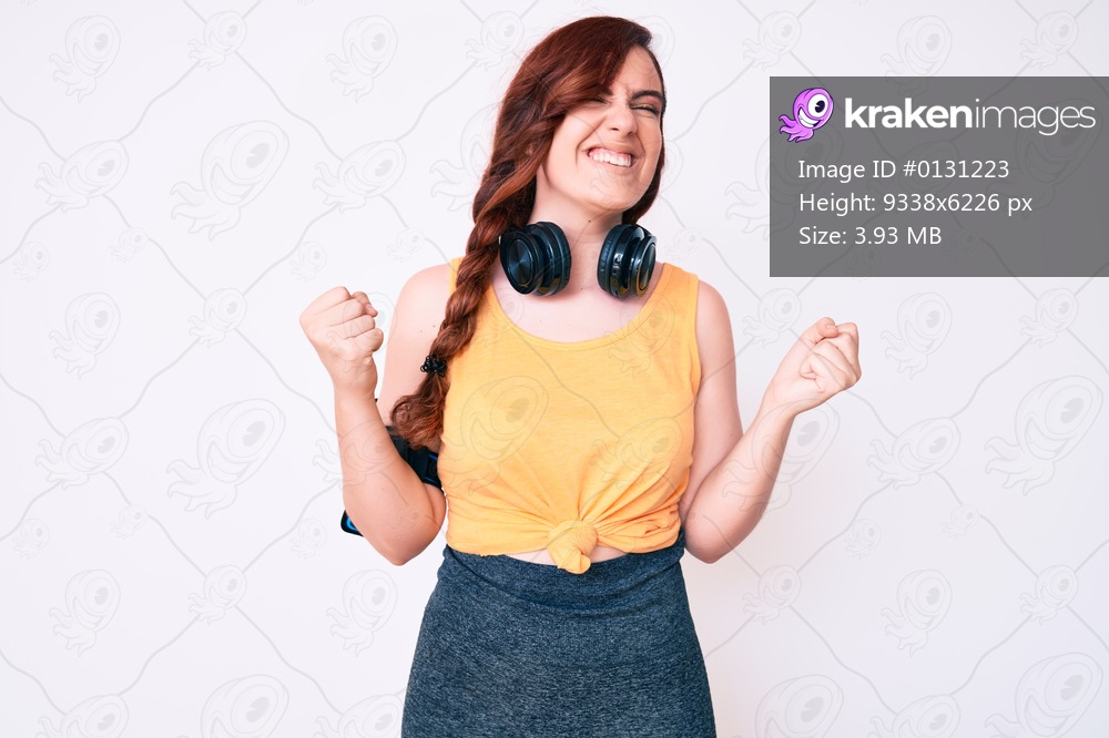 Young beautiful woman wearing gym clothes and using headphones very happy and excited doing winner gesture with arms raised, smiling and screaming for success. celebration concept. 