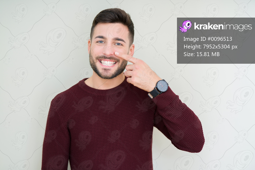 Young handsome man wearing a sweater over isolated background Pointing with hand finger to face and nose, smiling cheerful