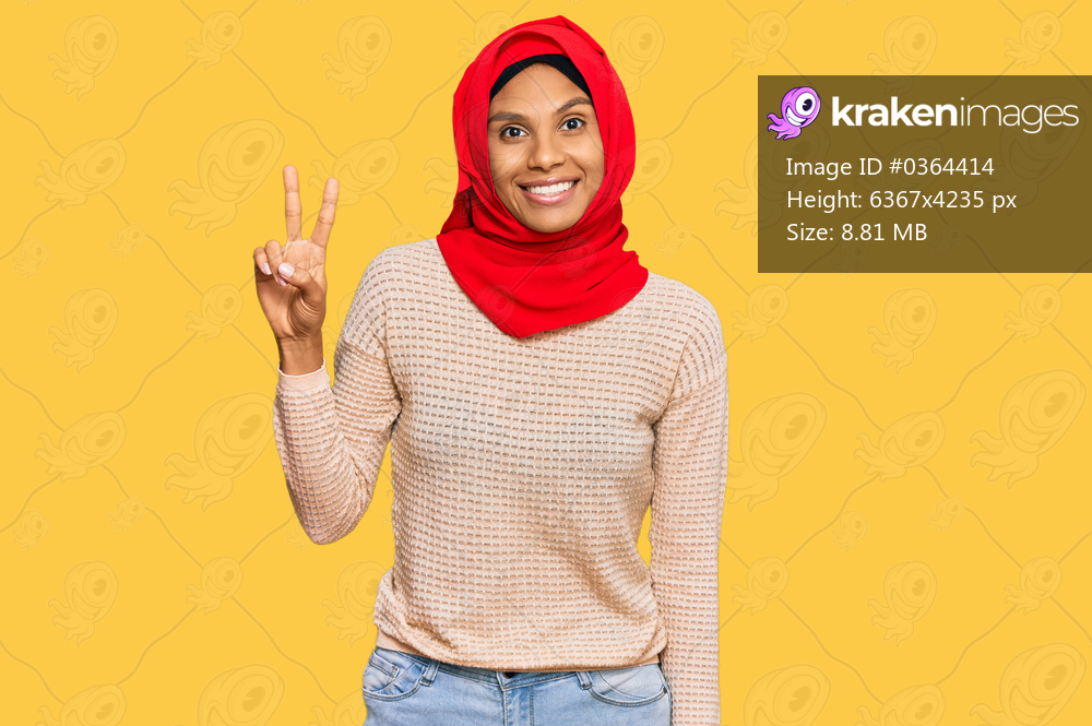 Young african american woman wearing traditional islamic hijab scarf smiling looking to the camera showing fingers doing victory sign. number two. 