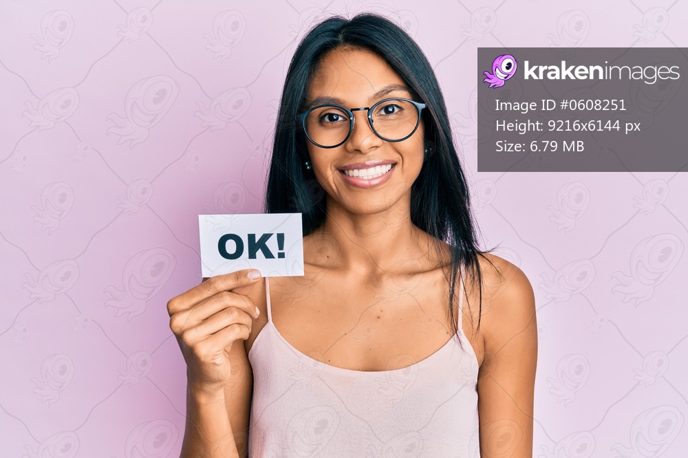 Young african american woman holding ok message paper looking positive and happy standing and smiling with a confident smile showing teeth 