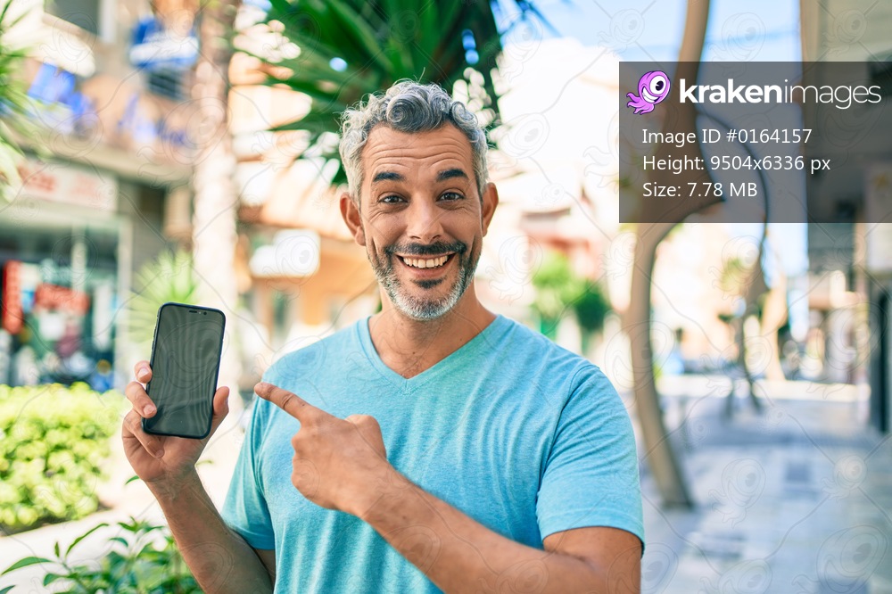 Middle age grey-haired man using smartphone at street of city smiling happy pointing with hand and finger 