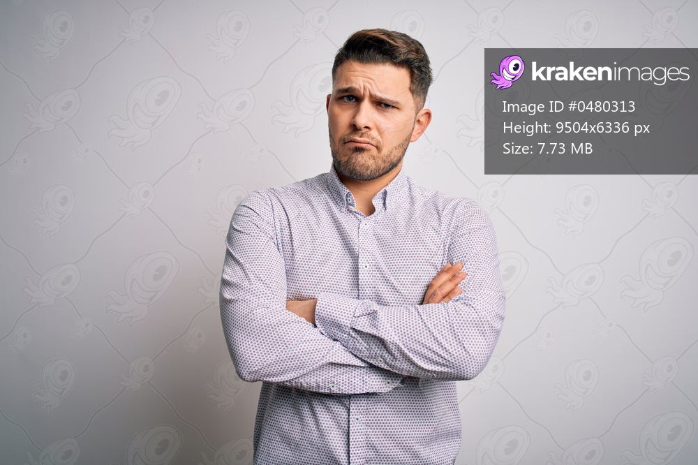 Young business man with blue eyes standing over isolated background skeptic and nervous, disapproving expression on face with crossed arms. Negative person.