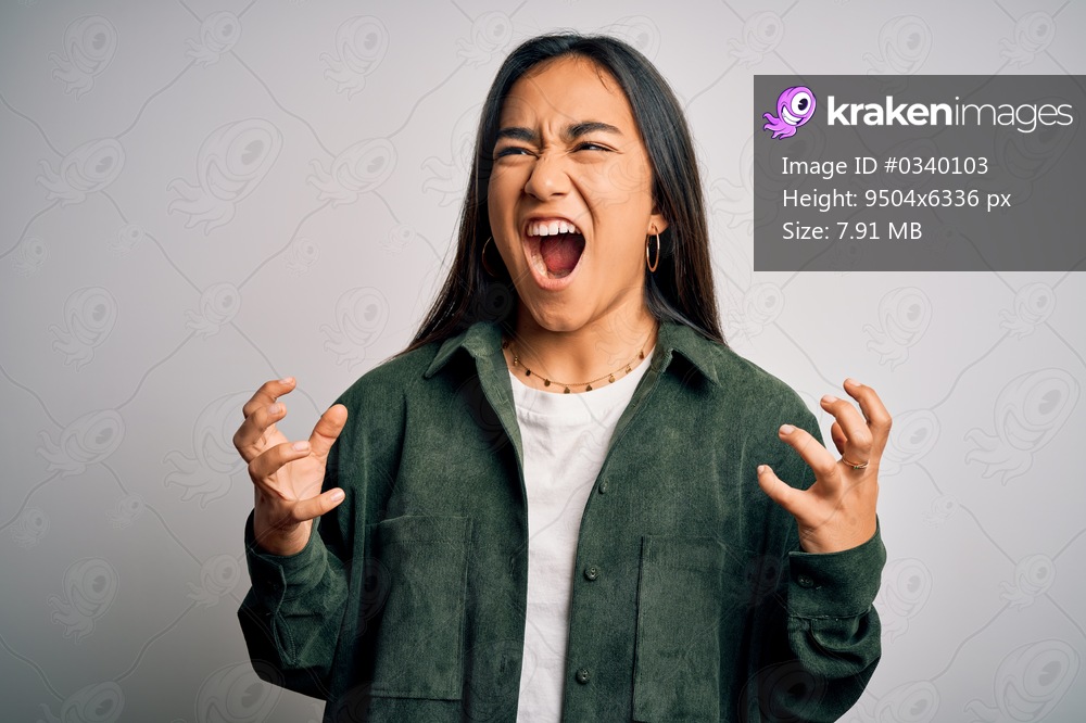 Young beautiful asian woman wearing casual shirt standing over isolated white background crazy and mad shouting and yelling with aggressive expression and arms raised. Frustration concept.